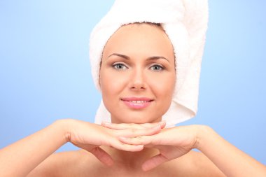 Beautiful young woman after shower with a towel on her head on blue background close-up