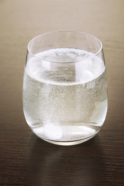 Verre avec comprimé effervescent dans l'eau avec bulles sur table en bois — Photo