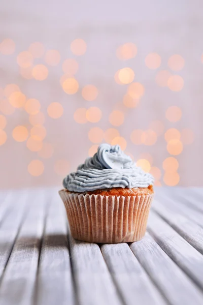 Cupcake saboroso com creme de manteiga, na mesa de madeira cor, no fundo luzes — Fotografia de Stock