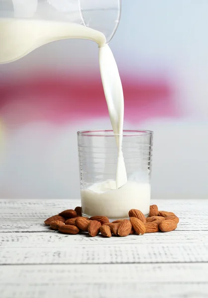Mandula-tejet öntenek, üveg, színes fából készült asztal, a világos háttér — Stock Fotó