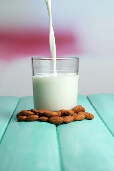 Mandelmilch wird in Glas gegossen, auf farbigem Holztisch, auf hellem Hintergrund — Stockfoto