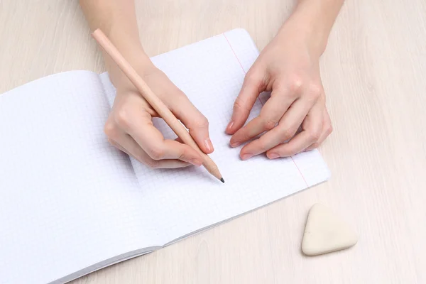 Human hands with pencil writing on paper and erase rubber on wooden table background — Stock Photo, Image