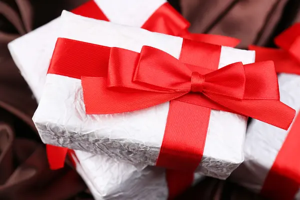 Beautiful gifts with red ribbons on silk background — Stock Photo, Image