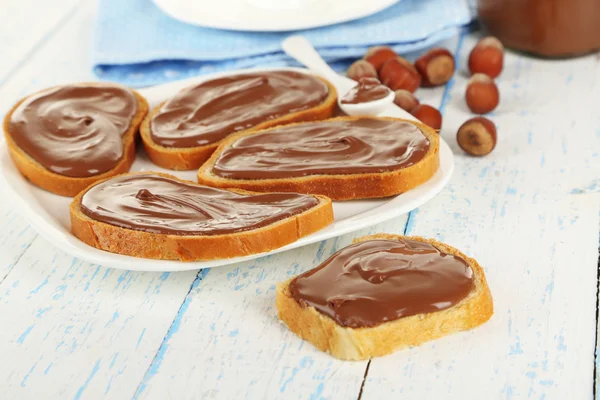 Roti dengan coklat hazelnut manis tersebar di atas piring di atas meja — Stok Foto