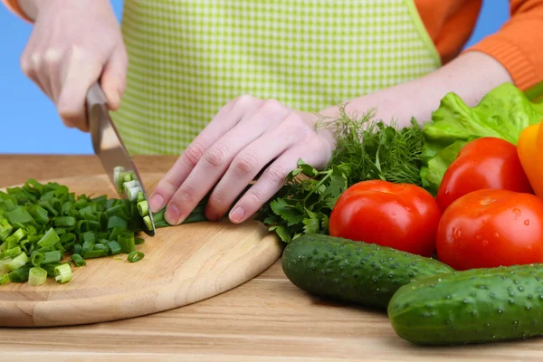 Frauenhände hacken Zwiebel auf Holzbrett, Nahaufnahme, auf blauem Hintergrund — Stockfoto