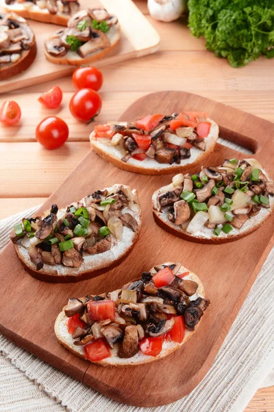 Delicious bruschetta with mushrooms on cutting board on table close-up — Stock Photo, Image