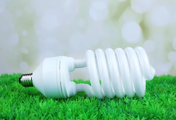 Ampoule à économie d'énergie sur herbe verte, sur fond de lumière — Photo