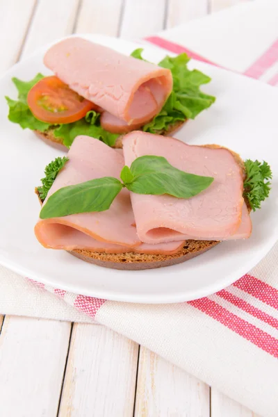 Läckra smörgåsar med sallad och skinka på tallriken på bordet närbild — Stockfoto