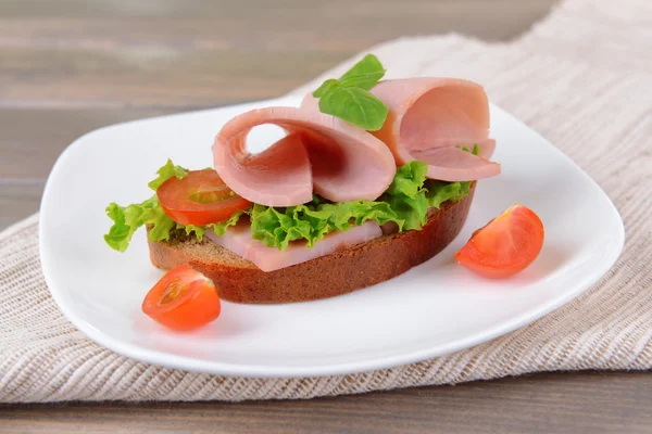 Sanduíche delicioso com alface e presunto na placa na mesa close-up — Fotografia de Stock