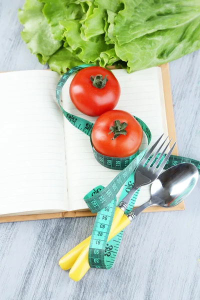 Cubertería atada con cinta métrica y libro con verduras sobre fondo de madera — Foto de Stock