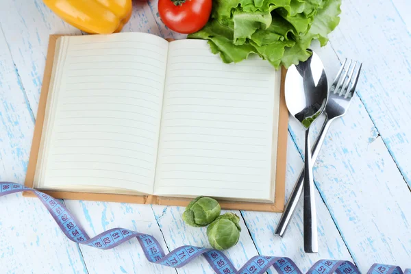 Livre avec couverts, ruban à mesurer et légumes sur fond bois — Photo