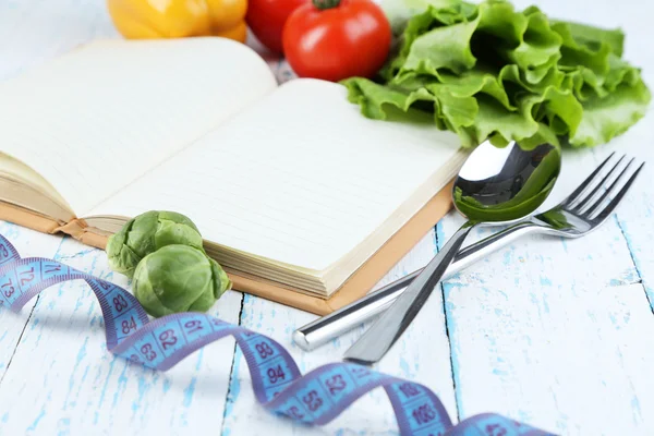 Libro con posate, metro a nastro e verdure su fondo di legno — Foto Stock