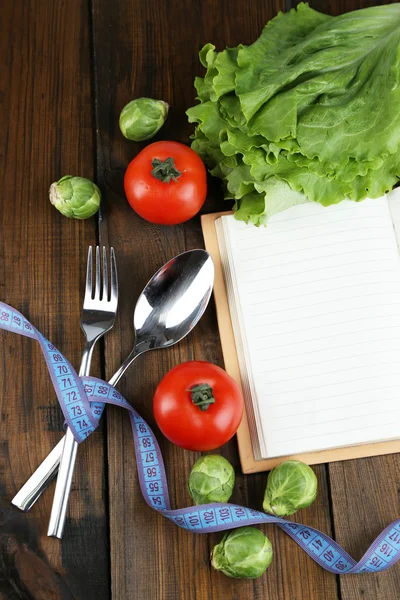 Couverts attachés avec ruban à mesurer et livre avec légumes sur fond en bois — Photo