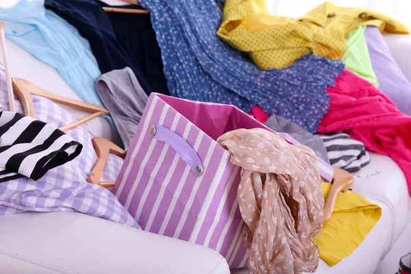 Rommelig kleurrijke kleding op sofa op lichte achtergrond — Stockfoto