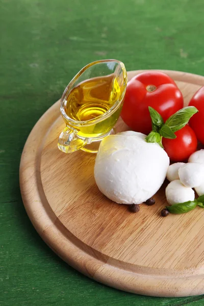 Composição com saborosas bolas de queijo mussarela, manjericão e tomates vermelhos, azeite na tábua de corte, na cor de fundo de madeira — Fotografia de Stock