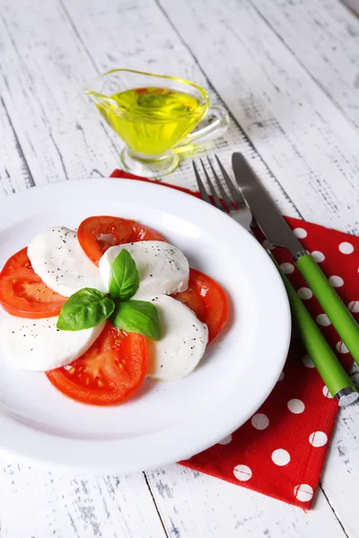 Caprese-Salat mit Mozarella, Tomaten und Basilikum auf Teller, auf Holztischhintergrund — Stockfoto