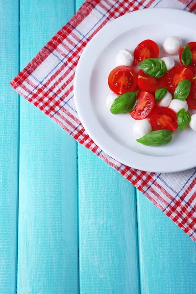 Ensalada Caprese con queso mozarella, tomates y albahaca en plato, sobre fondo de mesa de madera —  Fotos de Stock