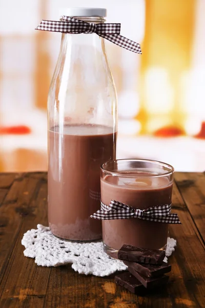 Lapte de ciocolată în sticlă și sticlă, pe masă de lemn, pe fundal luminos — Fotografie, imagine de stoc