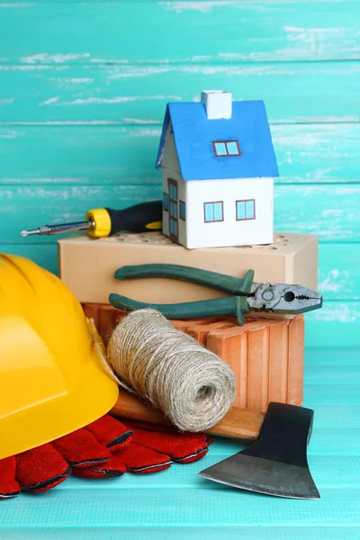 Composición con casco de seguridad, guantes de cuero, herramientas y casa decorativa sobre fondo de madera —  Fotos de Stock