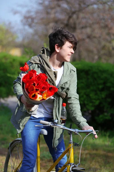 Jonge man met bloemen op fiets in park — Stockfoto