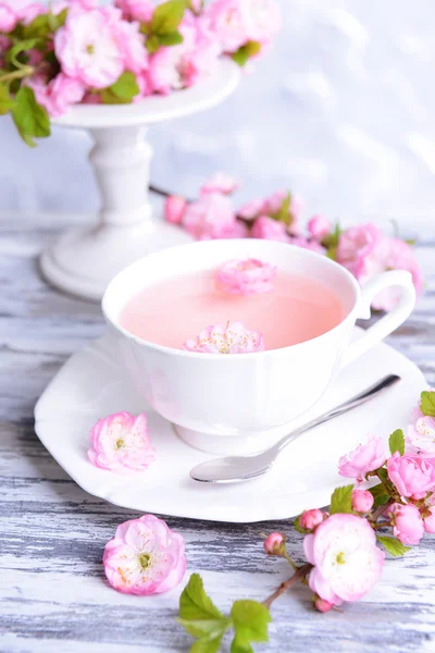 Beautiful fruit blossom with cup of tea on table on grey background — Stock Photo, Image