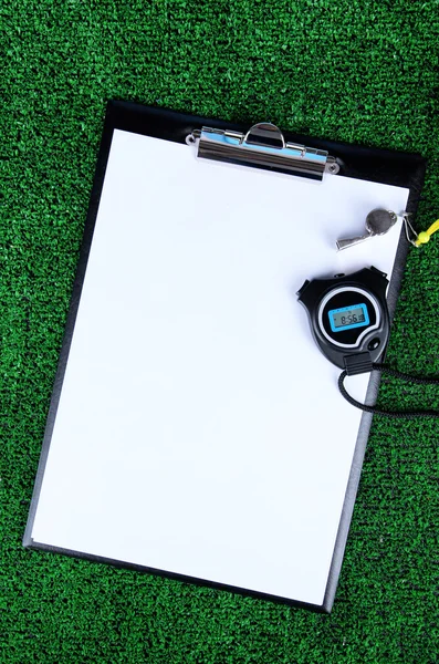 Sheet of paper, stopwatch and whistle on grass close-up — Stock Photo, Image