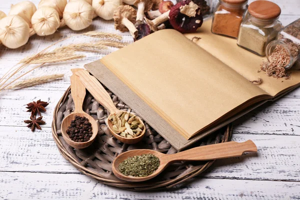 Diferentes especiarias e livro de cozinha na mesa de madeira, close-up — Fotografia de Stock