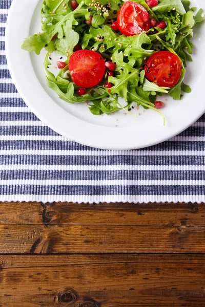 Grüner Salat mit Rucola, Tomaten und Sesam auf Teller, auf Holzgrund — Stockfoto