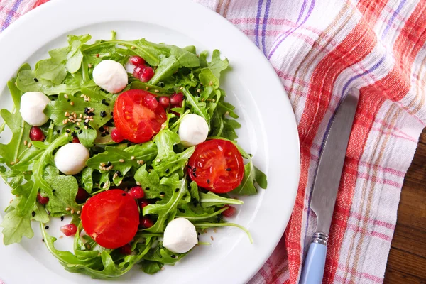 Ensalada verde hecha con rúcula, tomates, bolas de queso mozzarella y sésamo en plato, sobre fondo de madera — Foto de Stock