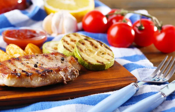 Grilovaný steak, grilovaná zelenina a smažené bramborové kousky na dřevěné desce na pozadí tabulky — Stock fotografie