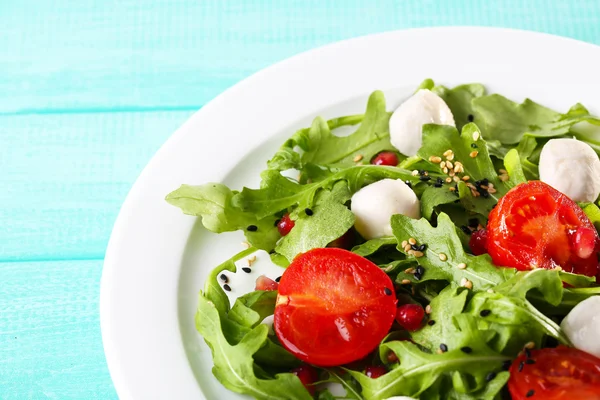 Zelený salát s rukolou, rajčaty, sýr mozzarella koule a sezam na desku, na barevné dřevěné pozadí — Stock fotografie