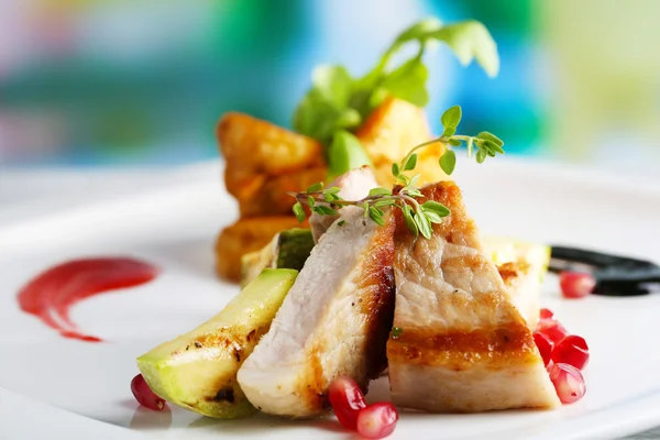 Grilled meat  with fried potato and marrow pieces and pomegranate seeds on plate, on wooden table on bright background — Stock Photo, Image