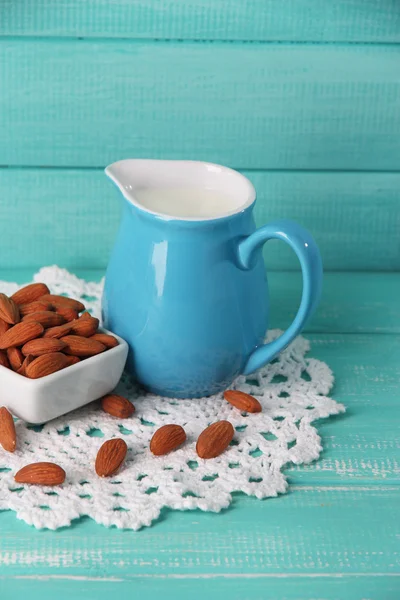 Almond milk in jug with almonds in bowl, on color wooden background — Stock Photo, Image