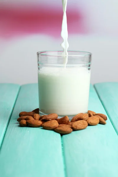 Mandelmilch wird in Glas gegossen, auf farbigem Holztisch, auf hellem Hintergrund — Stockfoto