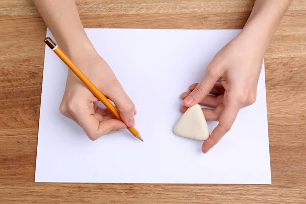 Mains humaines avec écriture au crayon sur papier et gomme le caoutchouc sur fond de table en bois — Photo