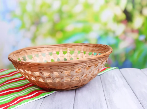 Empty wicker basket on wooden table, on bright background