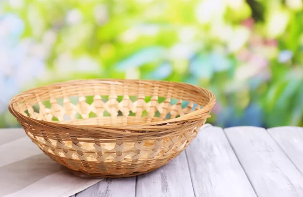 Empty wicker basket on wooden table, on bright background — Stock Photo, Image