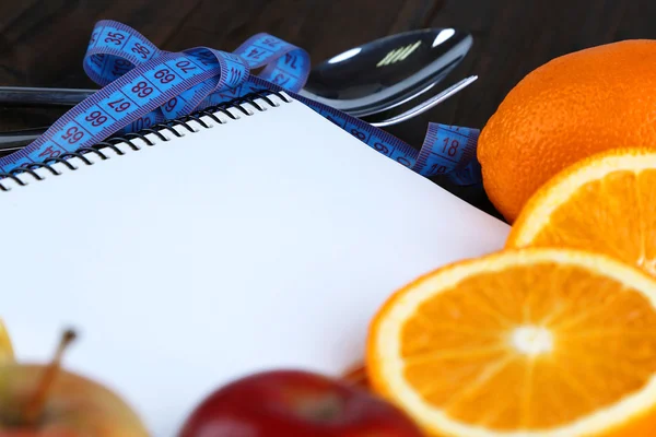 Cutlery tied with measuring tape and notebook with fruits on wooden background — Stock Photo, Image