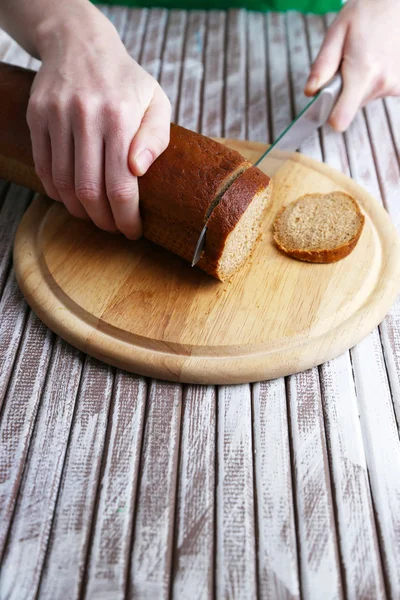 Manos femeninas cortando pan sobre tabla de madera, primer plano — Foto de Stock