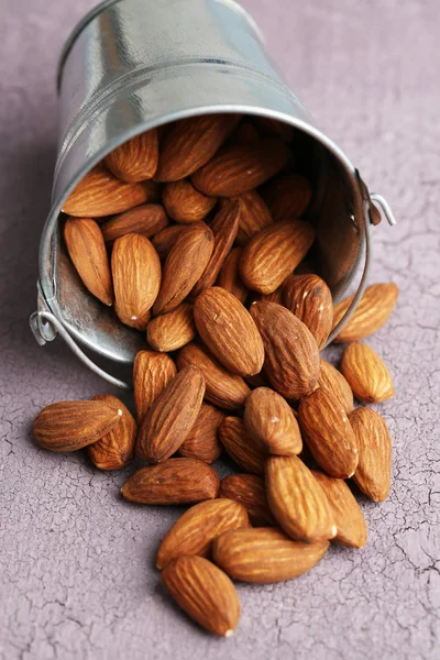 Almonds in bucket on color wooden background — Stock Photo, Image