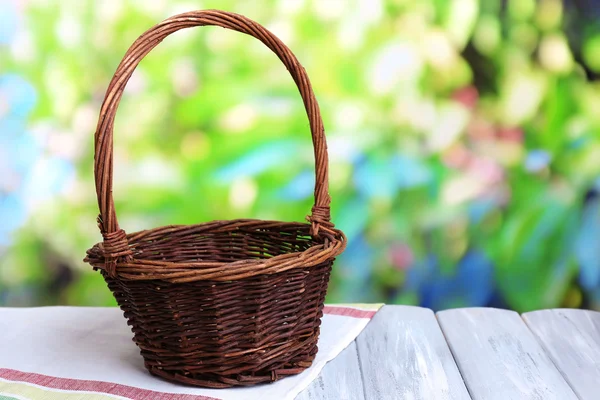 Empty wicker basket on wooden table, on bright background — Stock Photo, Image