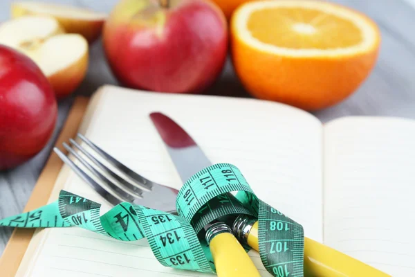 Bestikk knyttet til målebånd og bok med frukt på trebakgrunn – stockfoto