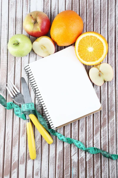 Besteck mit Maßband und Notizbuch mit Früchten auf Holzgrund gebunden — Stockfoto