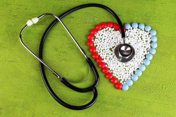 Heart of pills and stethoscope on wooden background — Stock Photo, Image