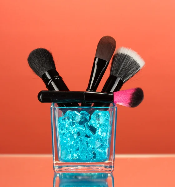 Make-up brushes in glass cup with stones on red background — Stock Photo, Image