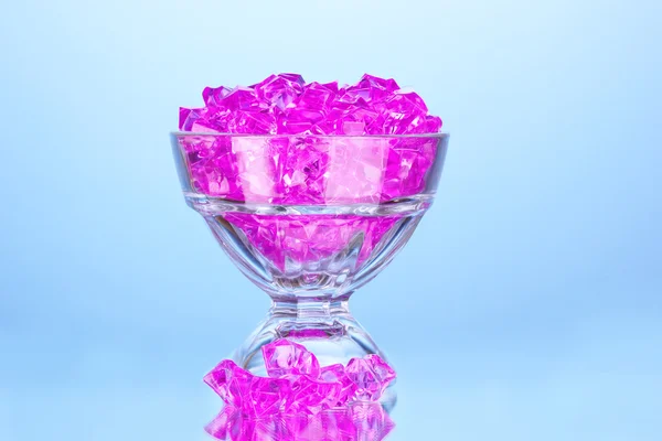 Een glas met roze decoratieve stenen op blauwe achtergrond close-up — Stockfoto