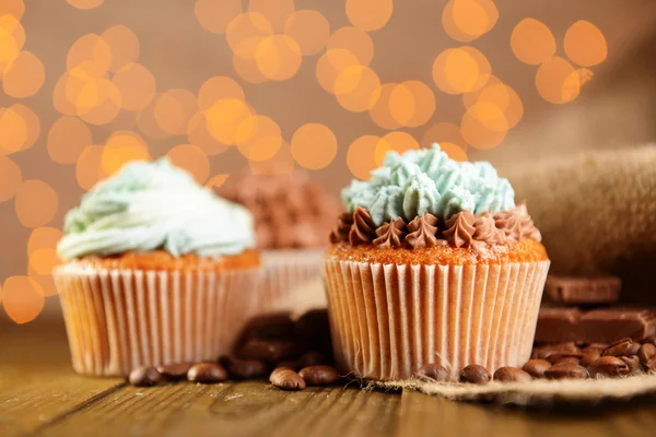 Cupcakes saborosos com creme de manteiga, na mesa de madeira, no fundo luzes — Fotografia de Stock