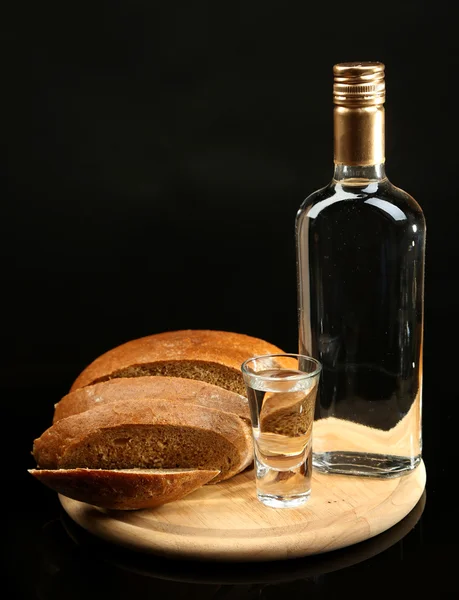 Garrafa de vodka, pão fresco e vidro em tábua de madeira, isolado em preto — Fotografia de Stock