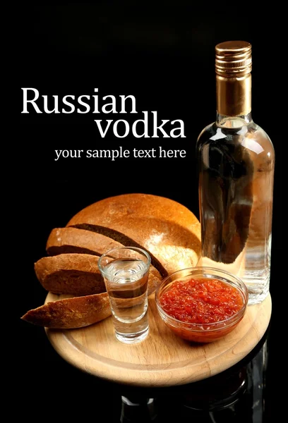 Láhev vodky, červený kaviár, čerstvý chléb na dřevěné desce, izolované na černém pozadí — Stockfoto