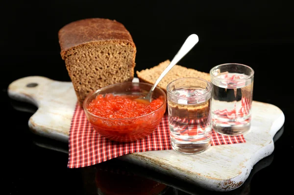 Состав со стаканами водки, красной икры, свежий хлеб на деревянной доске, изолированный на черном — стоковое фото